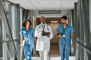 Senior doctor looking down at digital tablet, walking together with nurses in hospital corridor